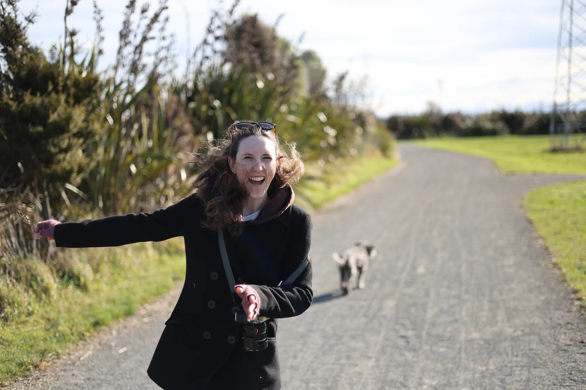 Caitlin laughs while carrying her camera on a sunny walk with Jasper behind her