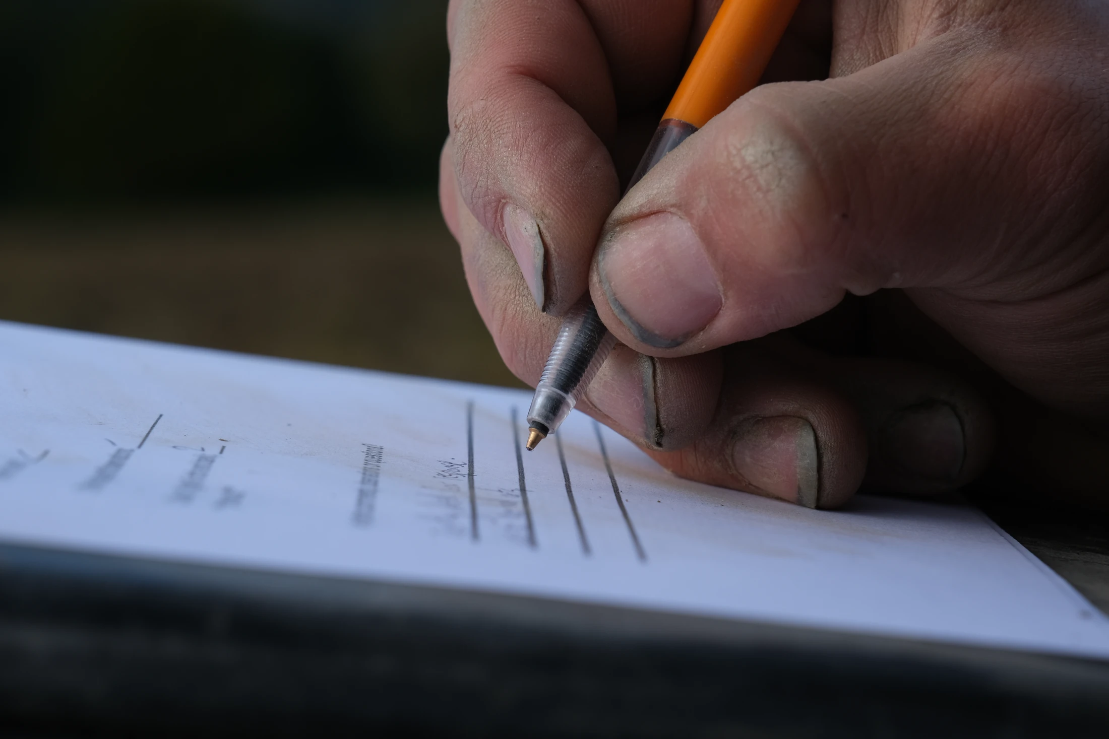 Soil-covered hands hold a pencil while making notes on a form
