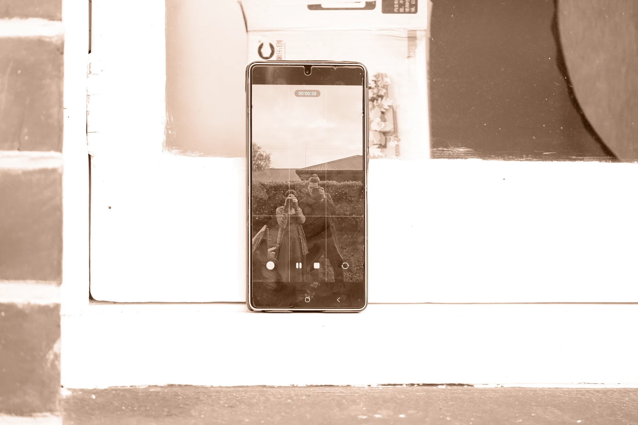 Two photographers appear together in the screen and reflection of a phone