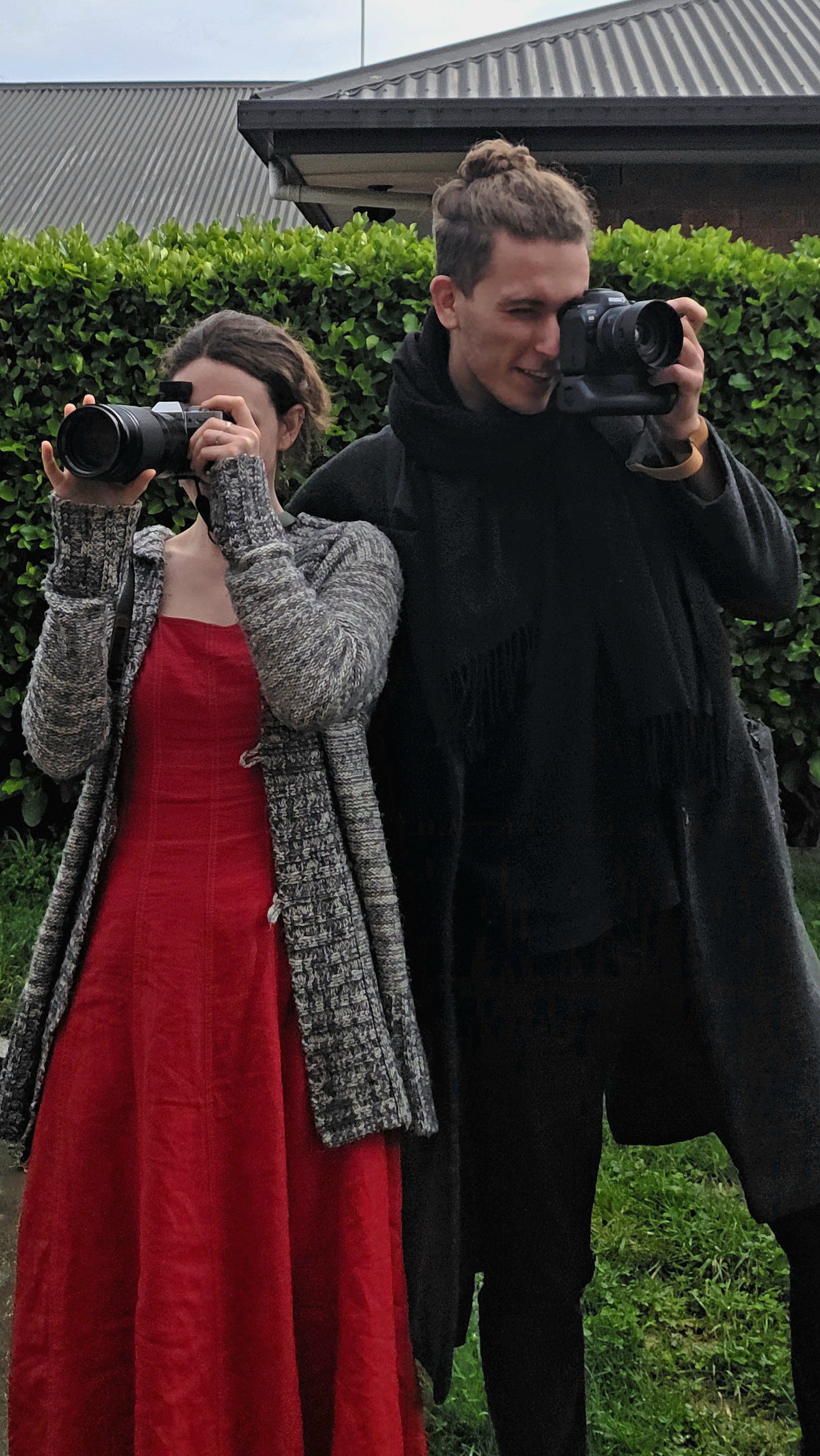 Caitlin and Kenan standing side by side with their cameras raised