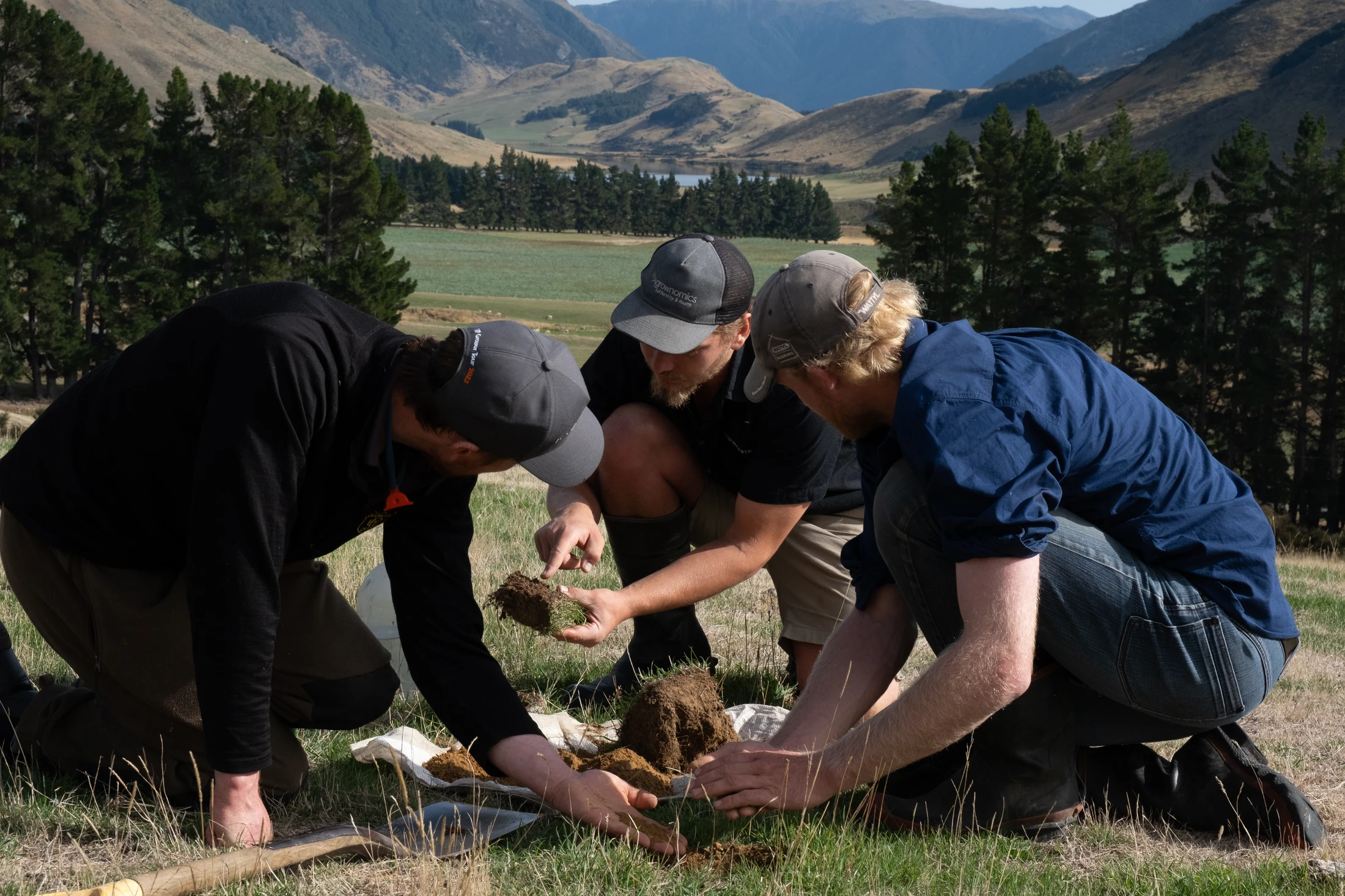 A group gathers in a field to inspect the soil with mountains in the distance