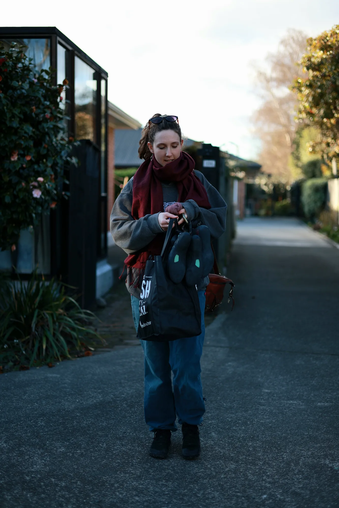 Caitlin looks down while arranging her bags on a sunlit residential lane