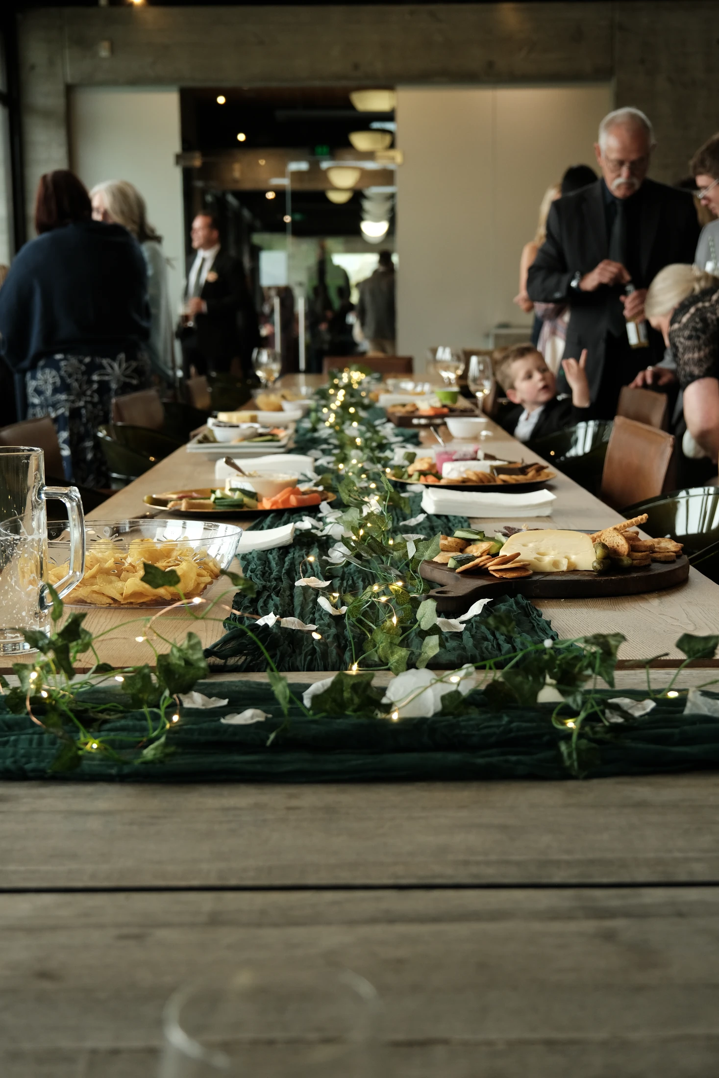A long wedding table dressed with green fabric, ivy, lights and shared platters
