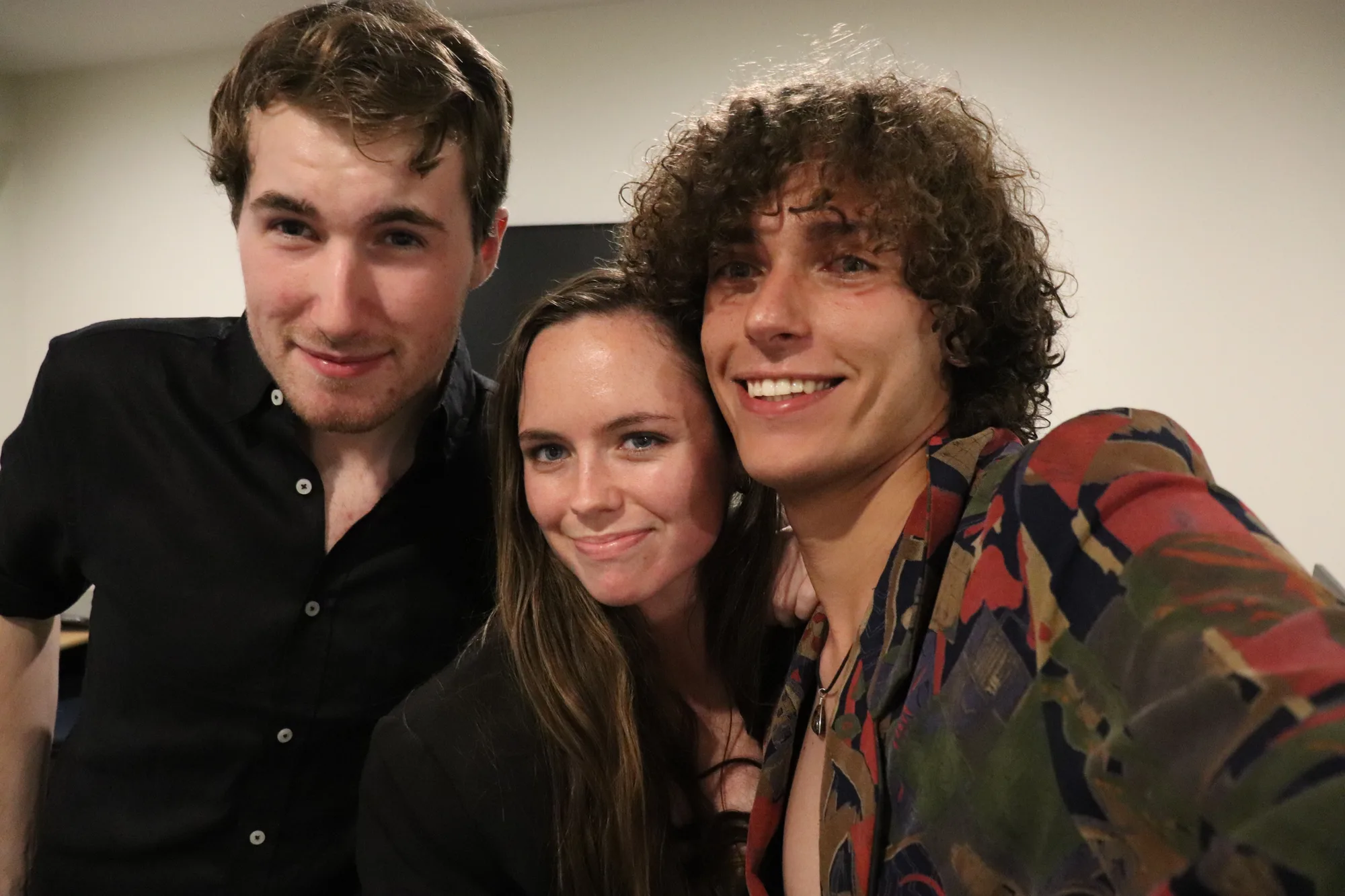 Kenan takes a selfie with two friends posing closely beside him indoors